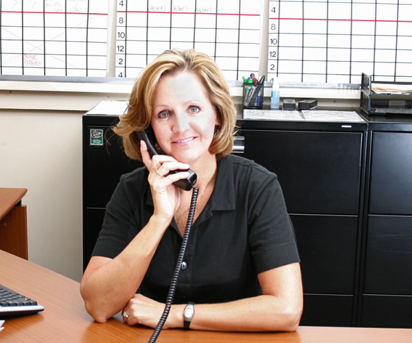 Woman with brown hair sitting at a desk and talking on telephone. Charts in the background