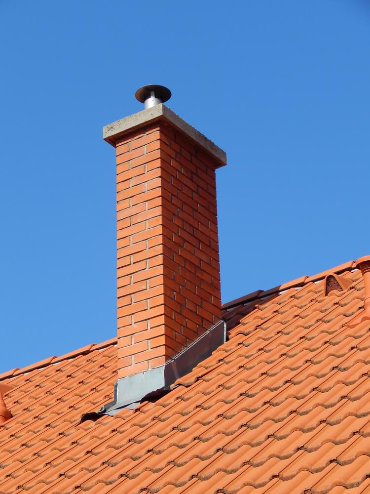 brick chimney with concrete crown and metal cap on orange stone tiled roof
